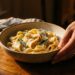 A warm bowl of comfort food on a pale surface in soft natural light, photographed from above