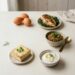 A variety of protein sources including eggs, grilled chicken, lentils, tofu, and Greek yoghurt arranged on a pale surface in natural light